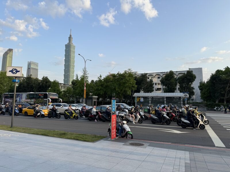 Des scooters attendent au feu rouge d'une rue de Taipei, avec la Taipei 101 en arrière-plan