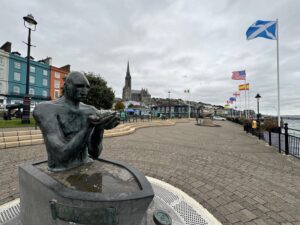 Vue sur la promenade le long du littoral de Cobh, dans le John F. Kennedy Park, avec au premier plan le monument "The Navigator" de Mary Gregoriy et à l'arrière-plan le Titanic Experience Cobh
