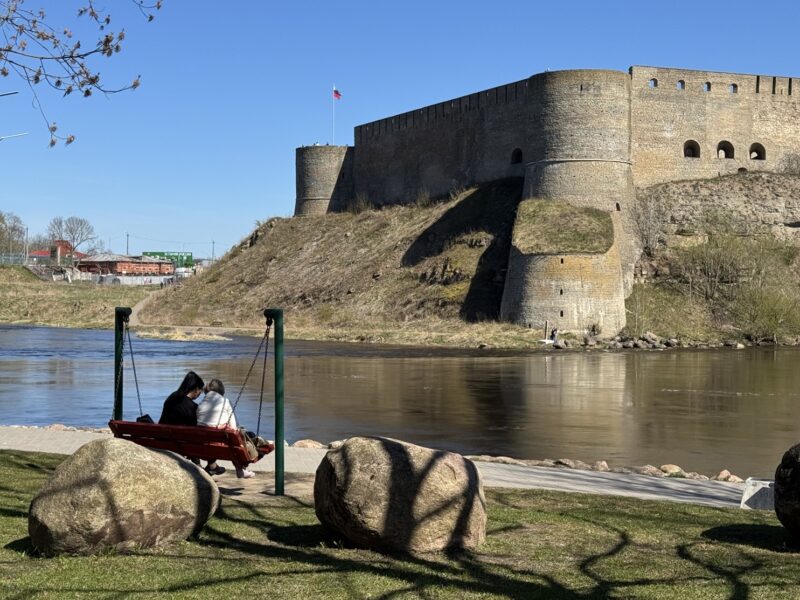 Des passants au bord du fleuve Narva, avec la forteresse d'Ivangorod (en Russie) de l'autre côté du fleuve